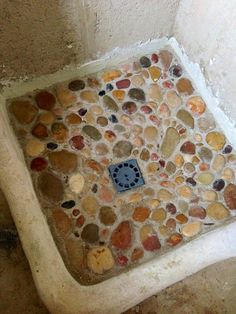 a bathroom with a stone floor and tile on the walls, including a blue square drain