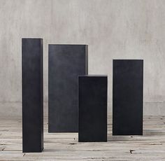 four tall black vases sitting next to each other on a wooden floor in front of a concrete wall