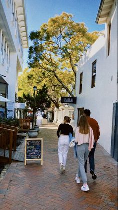 two people walking down the sidewalk in front of some white buildings with trees on either side