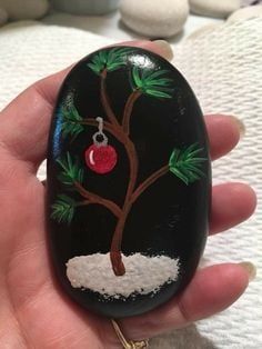 a hand is holding a painted rock with a tree and ornament on it