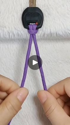 two hands are holding a purple rope with a hook on it and another hand is pulling the cord