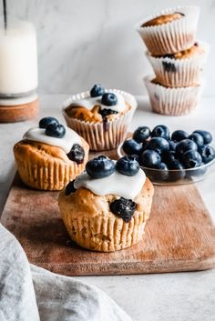 blueberry muffins with cream cheese frosting on a cutting board next to some fresh blueberries