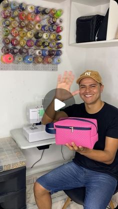 a man sitting in front of a sewing machine holding a pink case with his hand