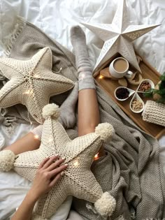 a woman laying on top of a bed next to two star shaped pillows and coffee