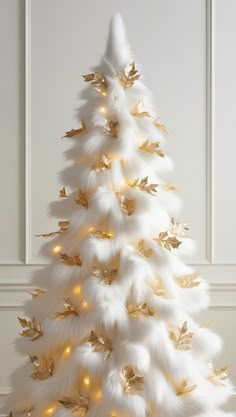 a white christmas tree with gold leaves and lights on the top, in front of a wall