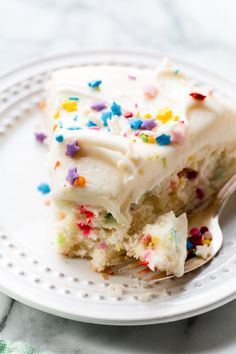 a piece of cake with white frosting and sprinkles on a plate