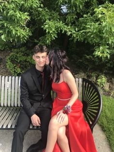 a young man and woman sitting on a bench in formal wear posing for the camera