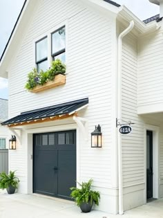 a white house with two black garage doors and plants on the windows sill above it