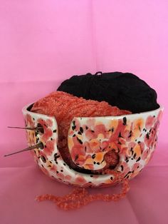 a bowl with yarn and knitting needles in it on a pink tablecloth covered surface