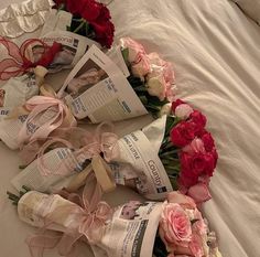 flowers and newspapers laid out on a bed with white sheets, pink ribbons and red roses