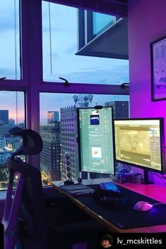 there is a desk with two monitors and a keyboard in front of a window overlooking the city