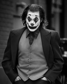 a man dressed in a suit and clown face makeup is posing for a black and white photo