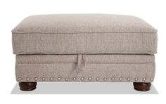 a beige ottoman with wooden legs and buttons on the bottom, in front of a white background