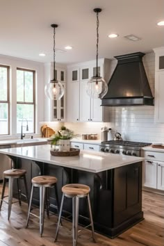 a kitchen island with stools in front of it and lights hanging from the ceiling