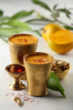 three gold cups filled with liquid sitting on top of a table next to lemons