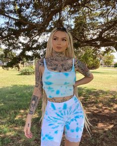 a woman with tattoos standing in front of a tree wearing blue and white tie dye shorts