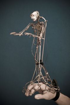 a human hand holding a wire skeleton with wires attached to it's back and arms