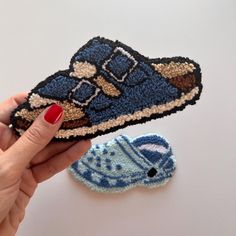 a hand is holding a small piece of knitted material next to a pair of shoes