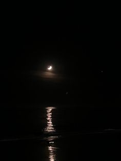 the moon is shining in the dark sky over the water at night with its reflection on the surface