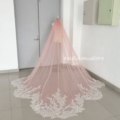 a pink wedding veil with white lace on the bottom sits in front of a doorway