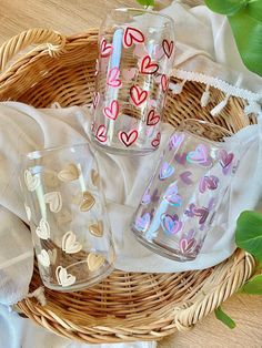 three glasses with hearts on them sitting in a basket next to some napkins and green leaves