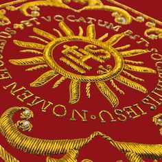 a red background with gold lettering and an image of a sun in the center on it