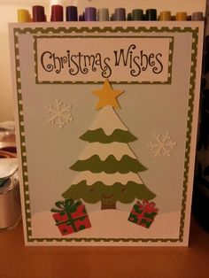 a handmade christmas card with a tree and presents on the bottom, surrounded by crayons