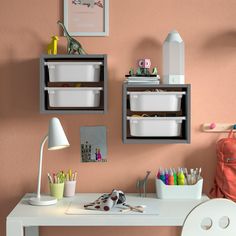 a white desk topped with two bins filled with crafting supplies next to a pink wall