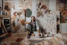 a woman is sitting on the floor in front of many pieces of art and painting