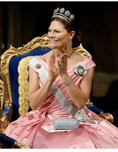 a woman wearing a tiara sitting in a chair with her hands clasped to her chest