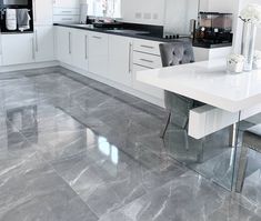 a modern kitchen with marble floors and white cabinetry is pictured in this image, there are two gray chairs at the table