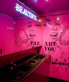 a bathroom with pink walls and graffiti on the wall, along with two sinks in front of it