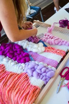 a woman is weaving yarn on a table with scissors and other crafting supplies in front of her