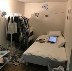 a bed room with a laptop on top of it next to a shelf filled with clothes