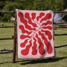 a red and white quilt hanging on a wooden fence in front of a green field