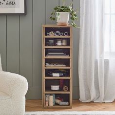 a wooden shelf filled with lots of crafting supplies next to a white chair and window