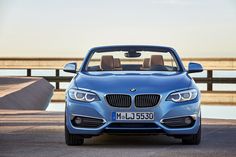 a blue convertible car parked next to a body of water with a bridge in the background