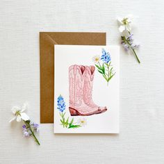 a card with a pink cowboy boot and blue flowers on it next to a brown envelope