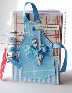 a small card with a blue apron and fork on it's pocket, holding utensils