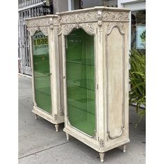 an old white armoire with green glass doors on the front and back sides, sitting outside