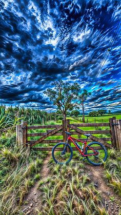 a bike parked in front of a wooden fence on the side of a dirt road