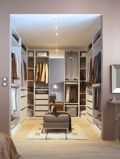 a walk in closet filled with lots of clothes and furniture next to a bed on top of a hard wood floor