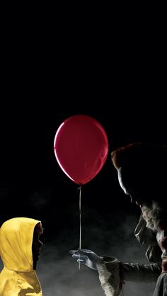 a person in a yellow raincoat holding a red balloon while another person in a yellow jacket looks on