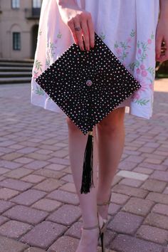 a woman in white dress holding a black and pink polka doted purse with tassels