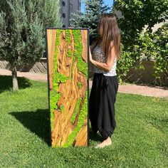 a woman standing next to a large piece of wood with green plants growing on it