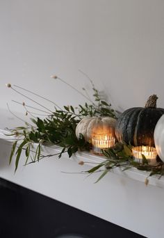 candles are sitting on the mantle with greenery and pumpkins in front of them