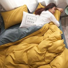 a woman laying on top of a bed covered in yellow and gray sheets with pillows