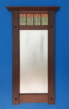 a mirror mounted to the side of a wooden frame on a blue wall with flowers and leaves painted on it