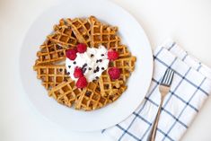 a white plate topped with waffles covered in whipped cream and raspberries