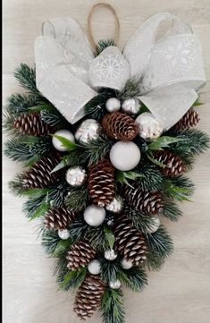 a christmas wreath with pine cones and white baubs on it, hanging from a wall